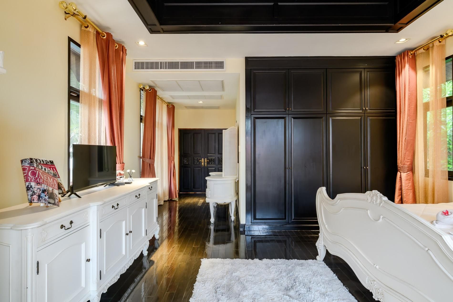A bedroom with a white bed, a dresser, a television, and a wardrobe.