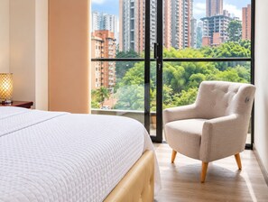 Ein Hotelzimmer mit einem Bett, einem Sessel, einem Nachttisch und einem Fenster mit Blick auf die Stadt.