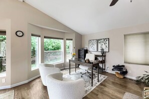 A spacious room with a desk, two chairs, a clock, and large windows. - Modern Lakeside Escape w/ Sauna + Mountain Access (Snohomish)