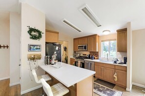 A modern kitchen with a central island, wooden cabinets, a microwave, and a refrigerator. - Modern Lakeside Escape w/ Sauna + Mountain Access (Snohomish)