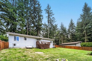 A single-story house with a fenced yard, surrounded by tall evergreen trees. - Modern Lakeside Escape w/ Sauna + Mountain Access (Snohomish)