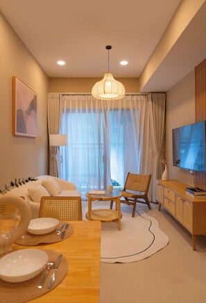 A modern living room with a sofa, dining table, chairs, a TV, and a large window with curtains. - Urban 2BR + 1BA | Central D1 | 500m Bui Vien (Thành phố Hồ Chí Minh)