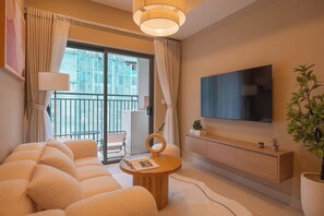 A modern living room with a sofa, a coffee table, a TV, and a balcony with a view of a building under construction. - High-Floor 2BR + 1BA | District 1 | Central City (Thành phố Hồ Chí Minh)