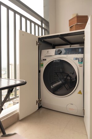 A compact, white front-loading washing machine with a control panel, a QR code, and a 10-year warranty sticker. - High-Floor 2BR + 1BA | District 1 | Central City (Thành phố Hồ Chí Minh)