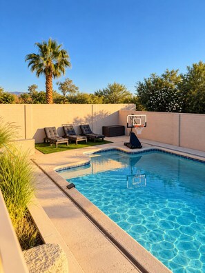 Ein Swimmingpool mit Basketballkorb, Liegestühlen und einer Palme.