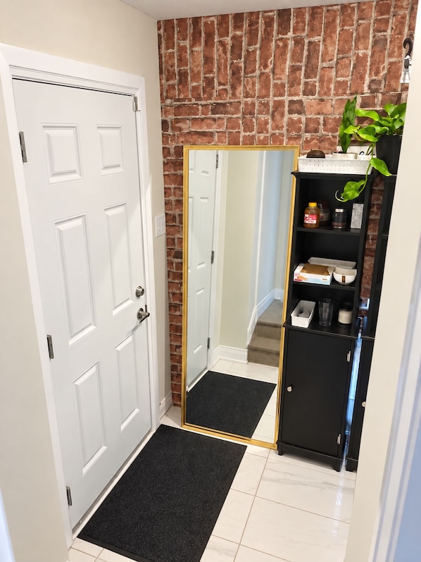 A hallway with a white door, a black mat, a mirror, and a black cabinet with shelves.