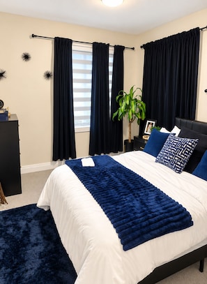 Ein Schlafzimmer mit einem Bett, dunklen Vorhängen, einem Blumentopf und einem Nachttisch.
