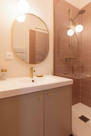A bathroom with a white sink, gold fixtures, a round mirror, and a shower with a glass door. - Charming Apartment 1br/2p - Lyon (Lyon)