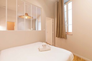 A hotel room with a bed, a window with curtains, a wall-mounted mirror, and a hanging light fixture. - Charming Apartment 1br/2p - Lyon (Lyon)