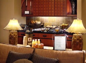 Eine Hotelküche mit Buffet, darunter Brot, Gebäck und Getränke. An beiden Seiten der Theke befinden sich Lampen, und ein Menüschild ist sichtbar.