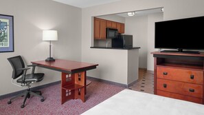 Ein Hotelzimmer mit Holztisch, Stuhl, Fernseher, einer Küchenzeile und einem Bett.