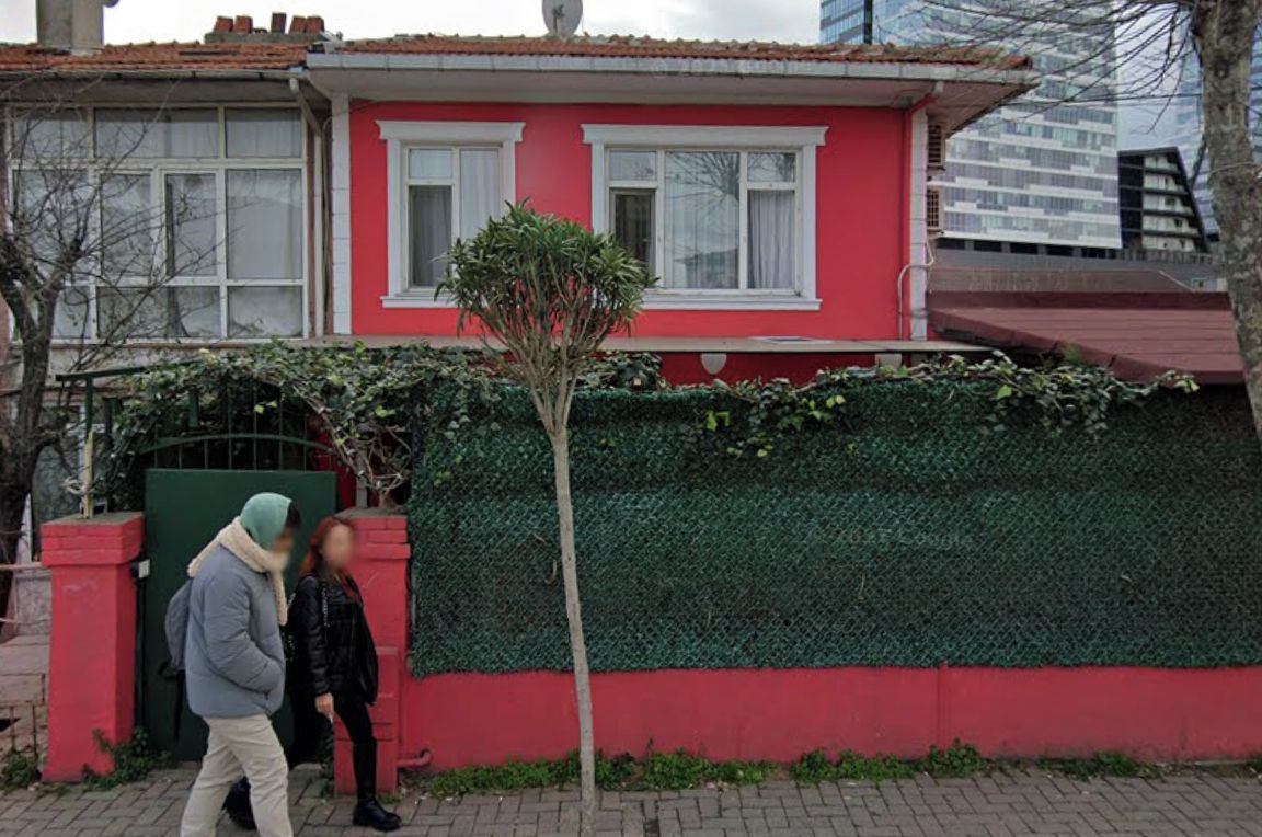 A red building with two windows and a green hedge.