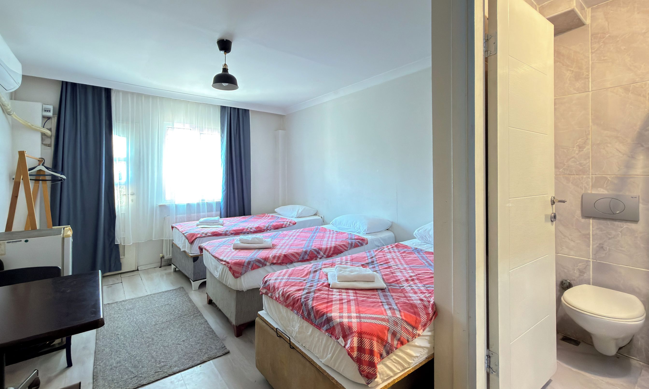 A hotel room with three beds, a desk, a chair, a radiator, and a bathroom.