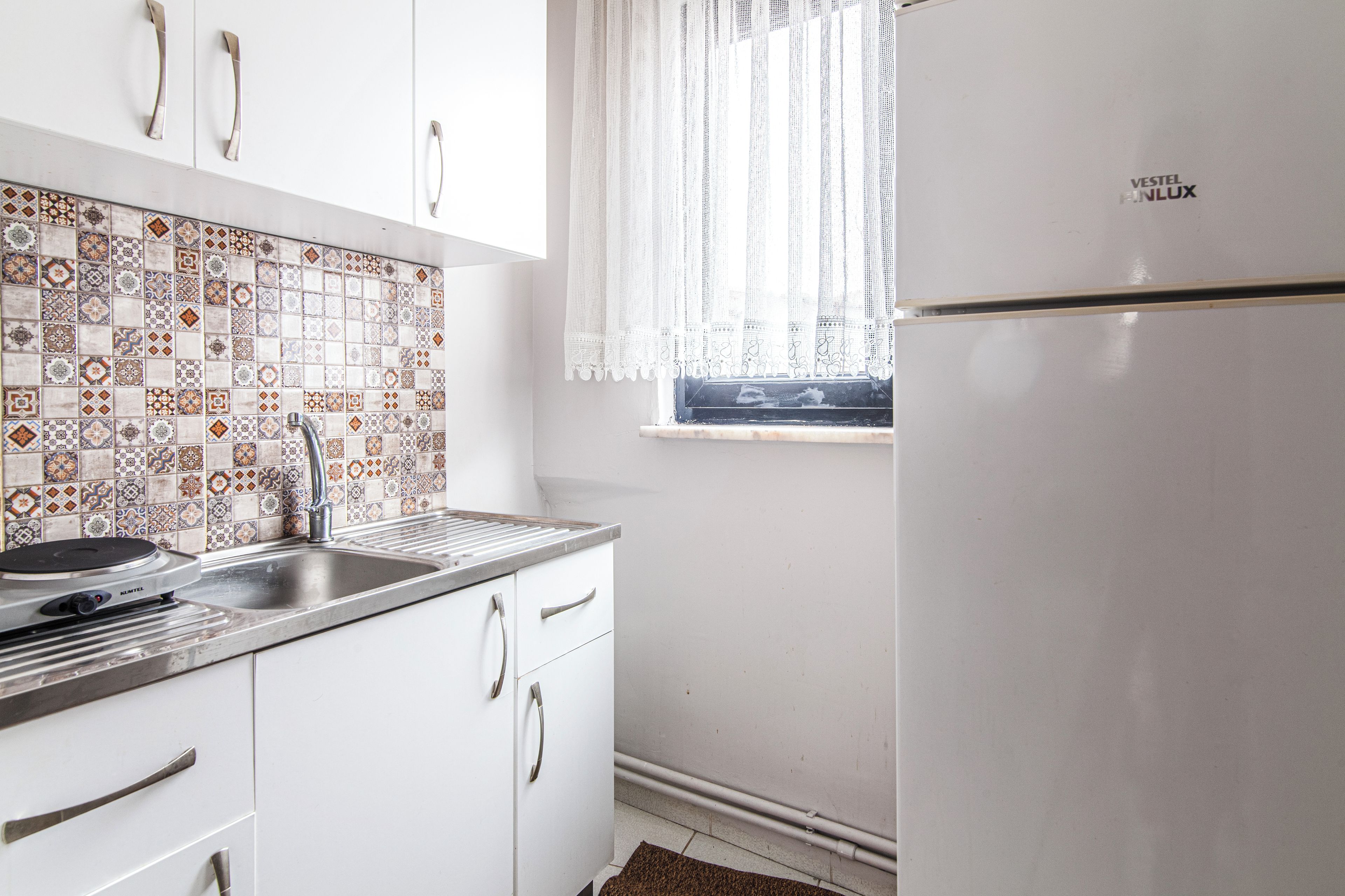 A kitchen with white cabinets, a stainless steel sink, and a tiled backsplash.