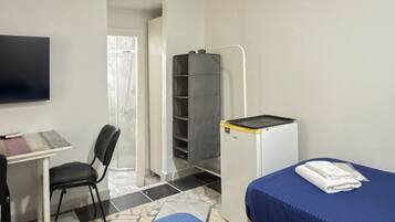 A hotel room with two beds, a desk, a chair, a television, and a small kitchenette.