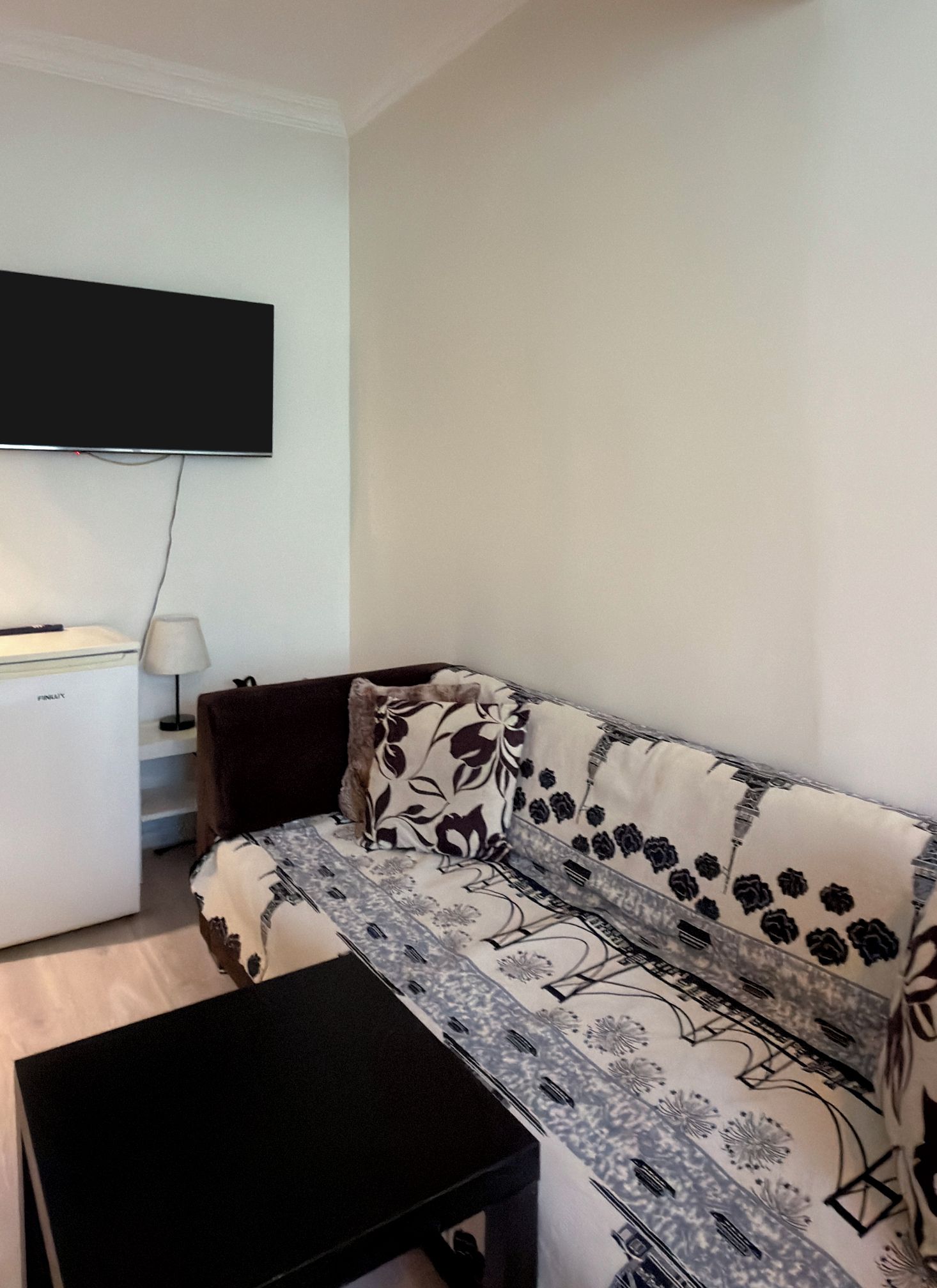 Un salon comprenant un canapé, un téléviseur à écran plat fixé au mur, une petite table et une lampe.