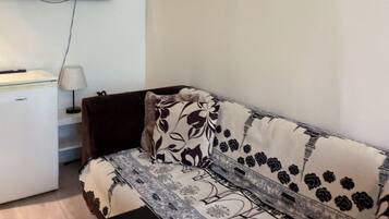 Un salon comprenant un canapé, un téléviseur à écran plat fixé au mur, une petite table et une lampe.