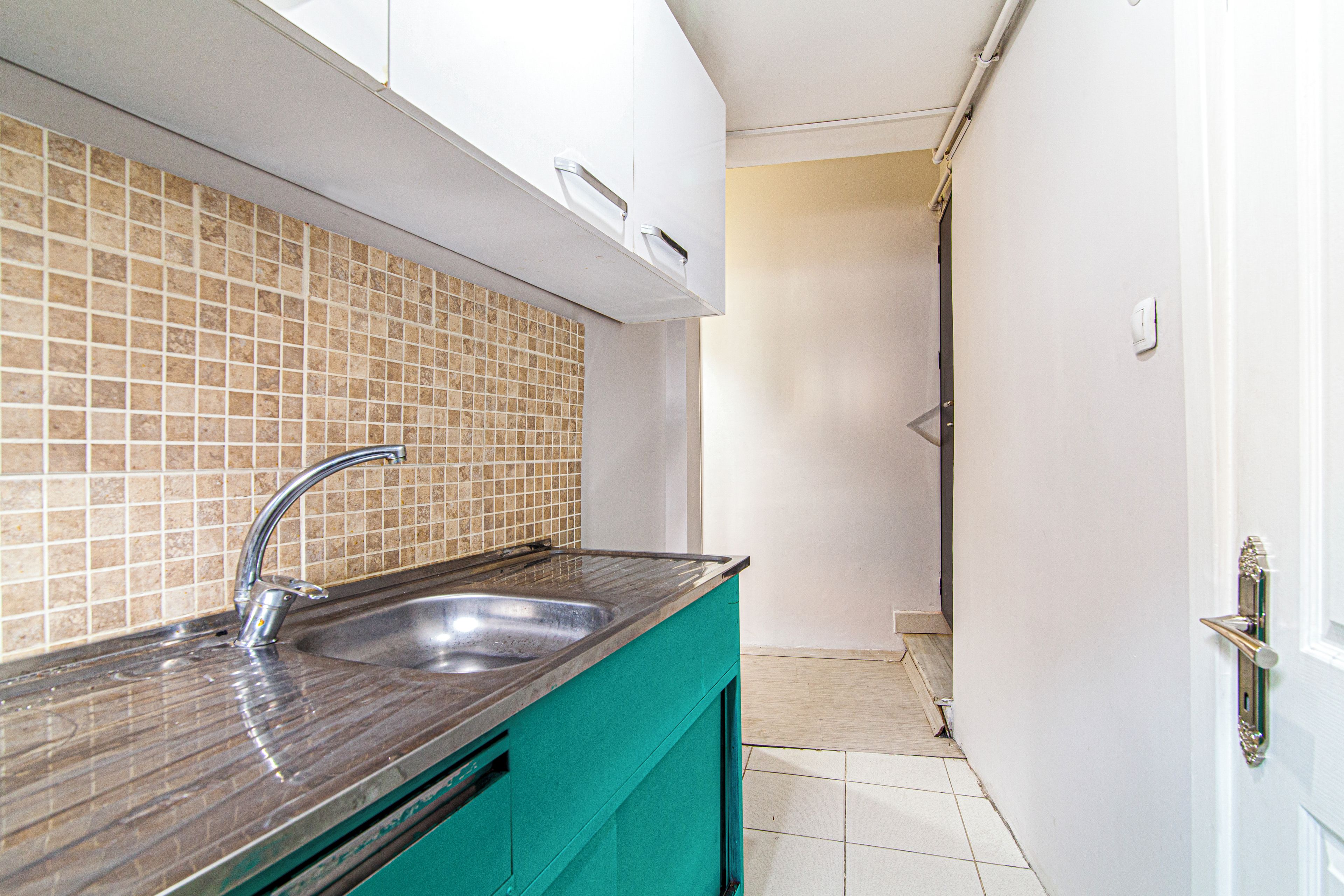 A kitchen with a stainless steel sink, a tiled backsplash, and a teal-colored countertop.