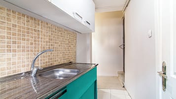 A kitchen with a stainless steel sink, a tiled backsplash, and a teal-colored countertop.