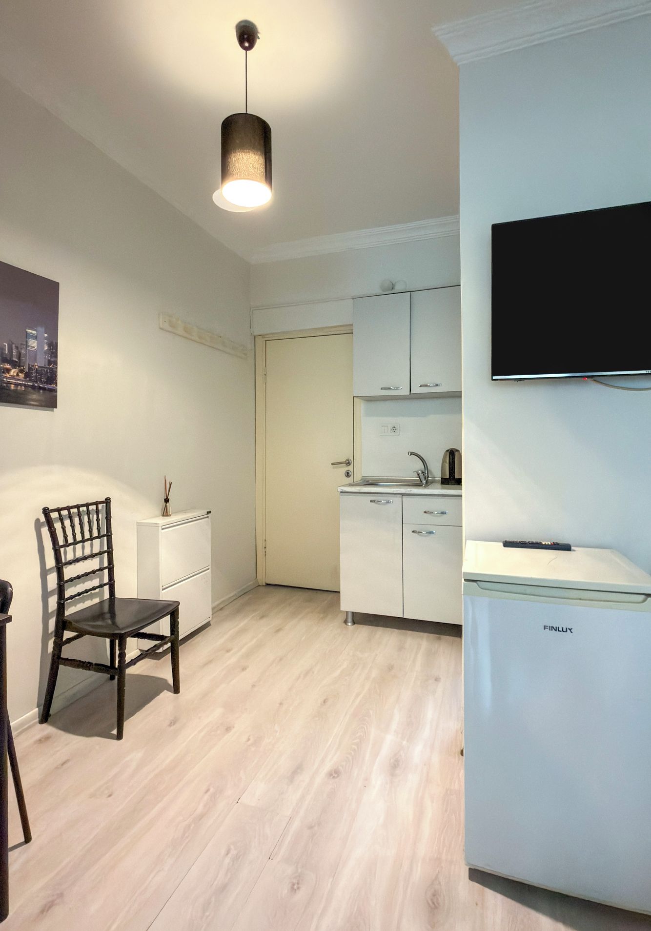 A compact kitchen with a built-in dishwasher, a dining area with a wooden chair, and a flat-screen TV mounted on the wall.