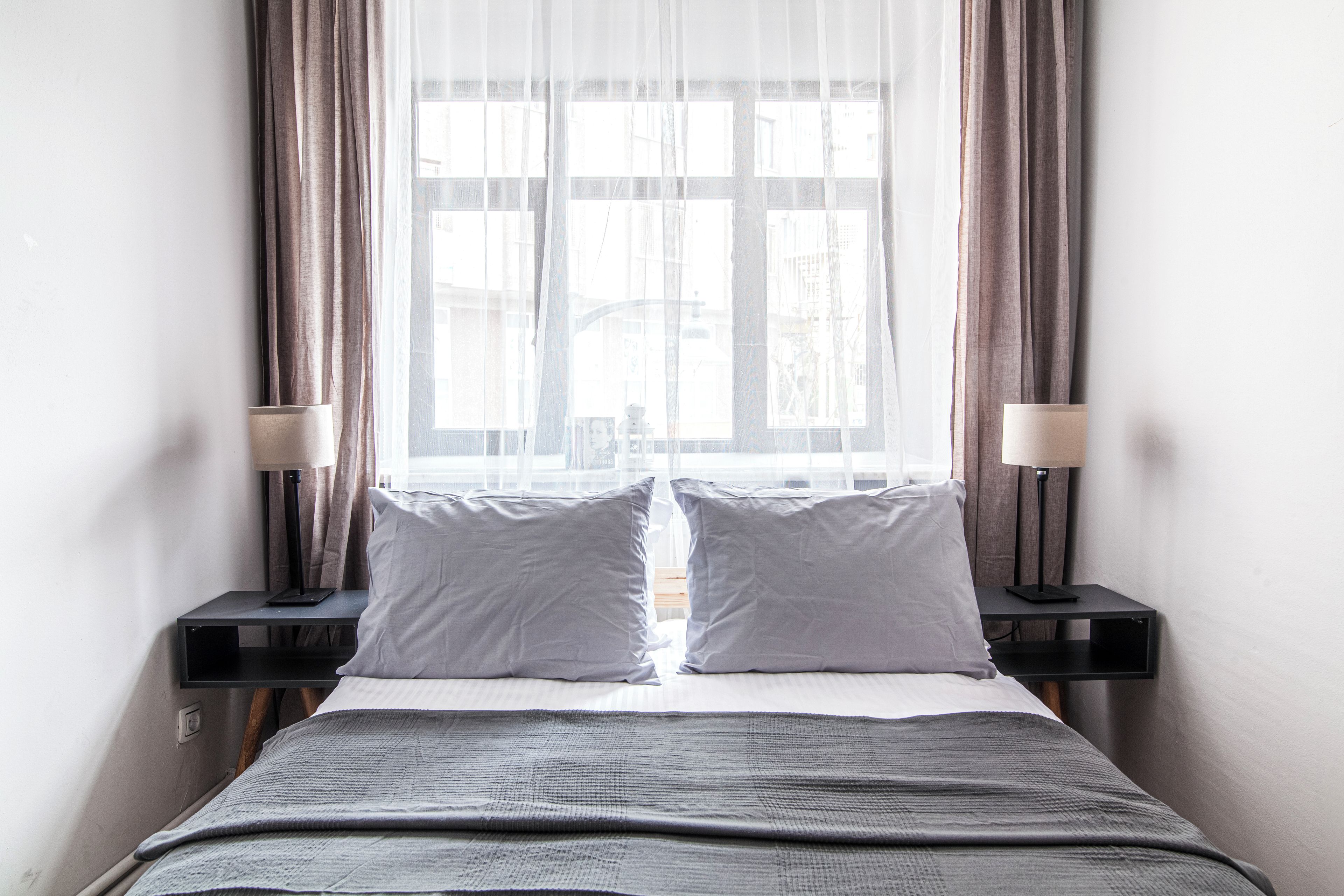 A hotel room with a bed, two bedside lamps, and a window with curtains.