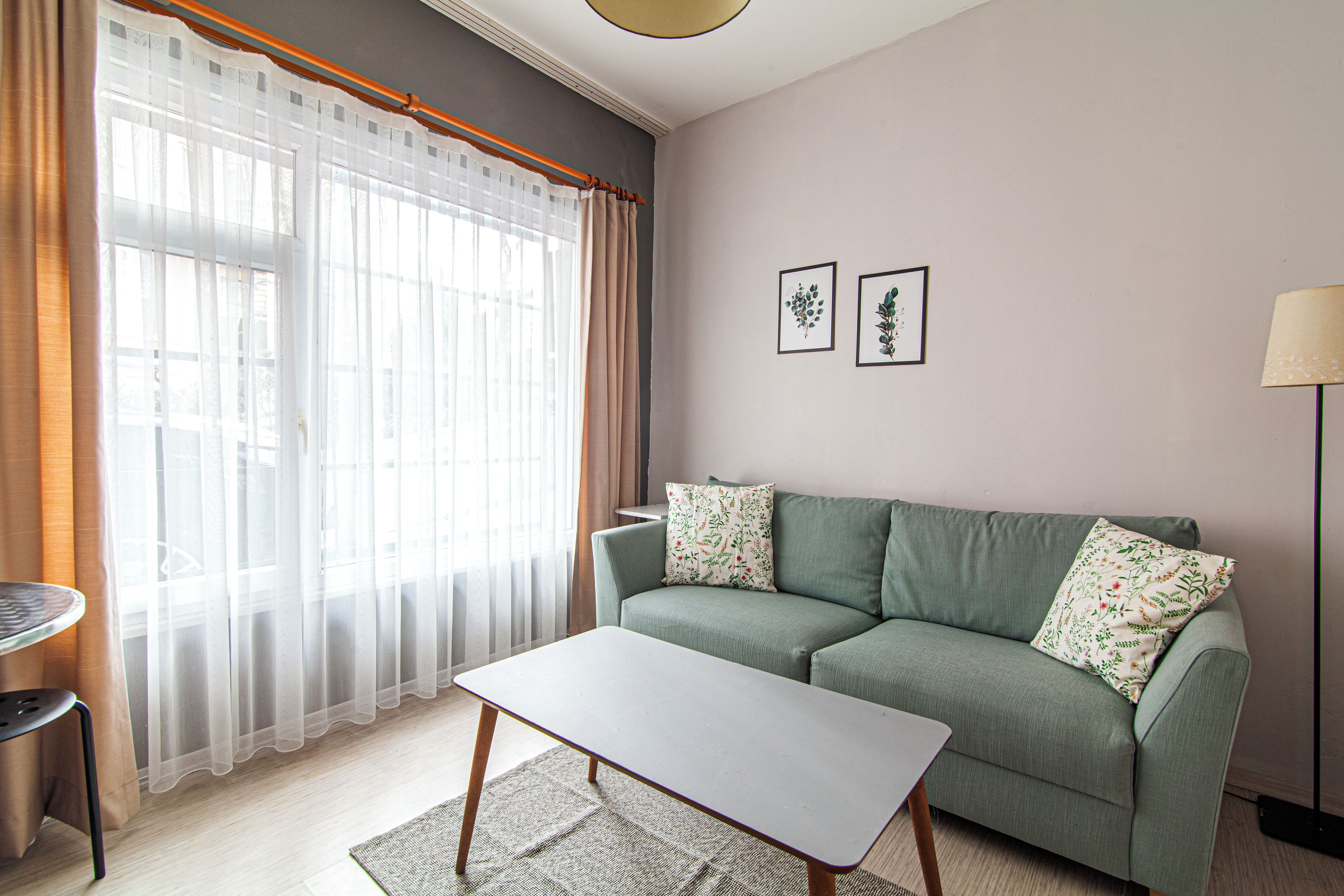 Una sala de estar con un sofá, una mesita de centro, una lámpara y una ventana con cortinas traslúcidas.