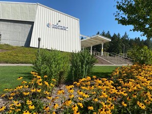 Ein Gebäude mit dem Schild "Tualatin Hills Athletic Center", mit überdachter Einfahrt und einer Rasenfläche mit gelben Blumen im Vordergrund.