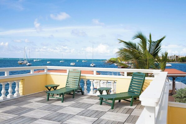 Ein Balkon mit zwei grünen Stühlen und einem kleinen Tisch mit Blick auf einen Yachthafen und mehreren Booten.