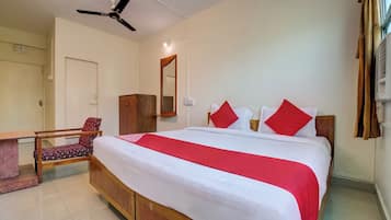A hotel room with a bed, a desk, a chair, a ceiling fan, and a window with curtains.