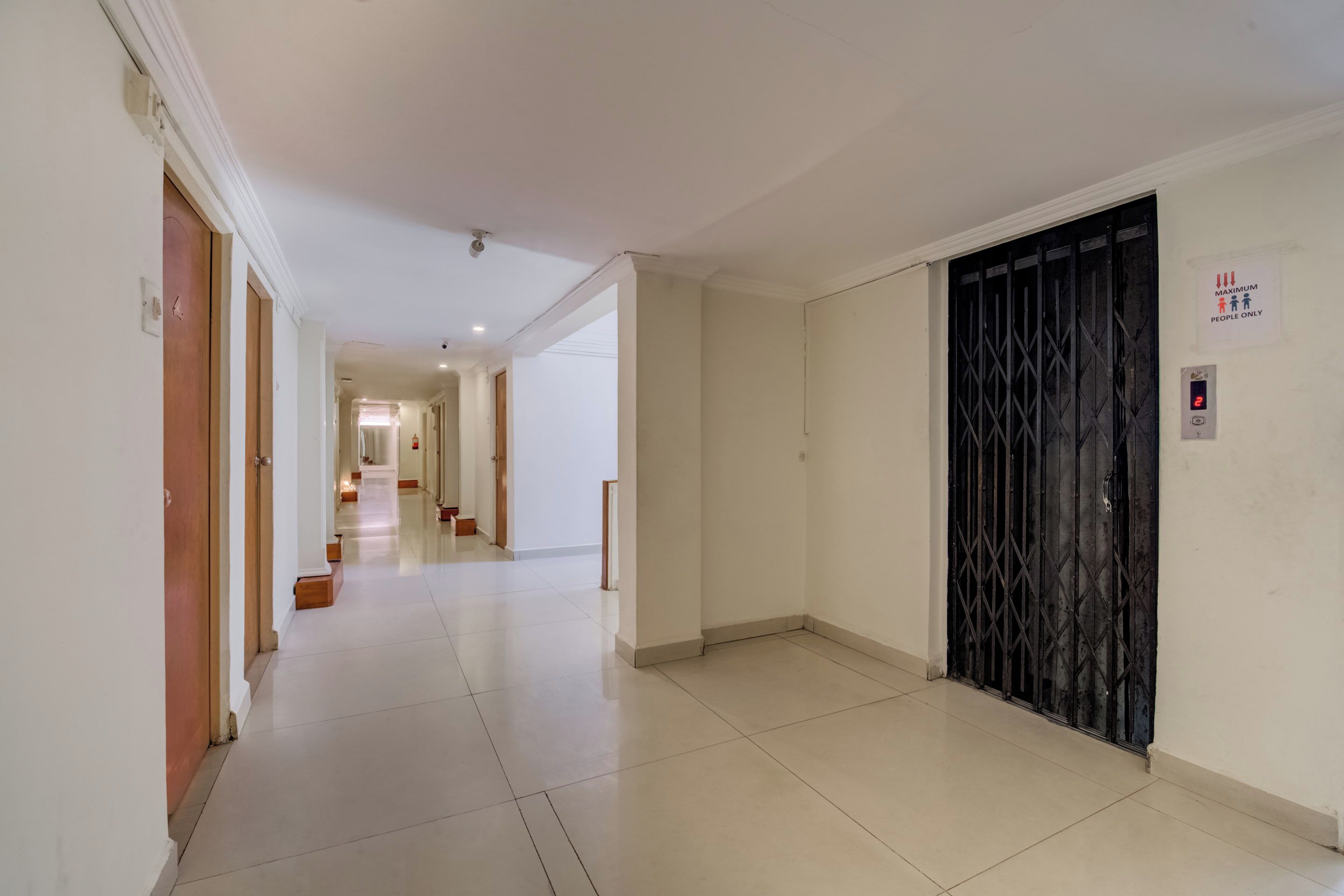 A hotel corridor with a black metal gate, a maximum occupancy sign, and a digital display showing the number 2.