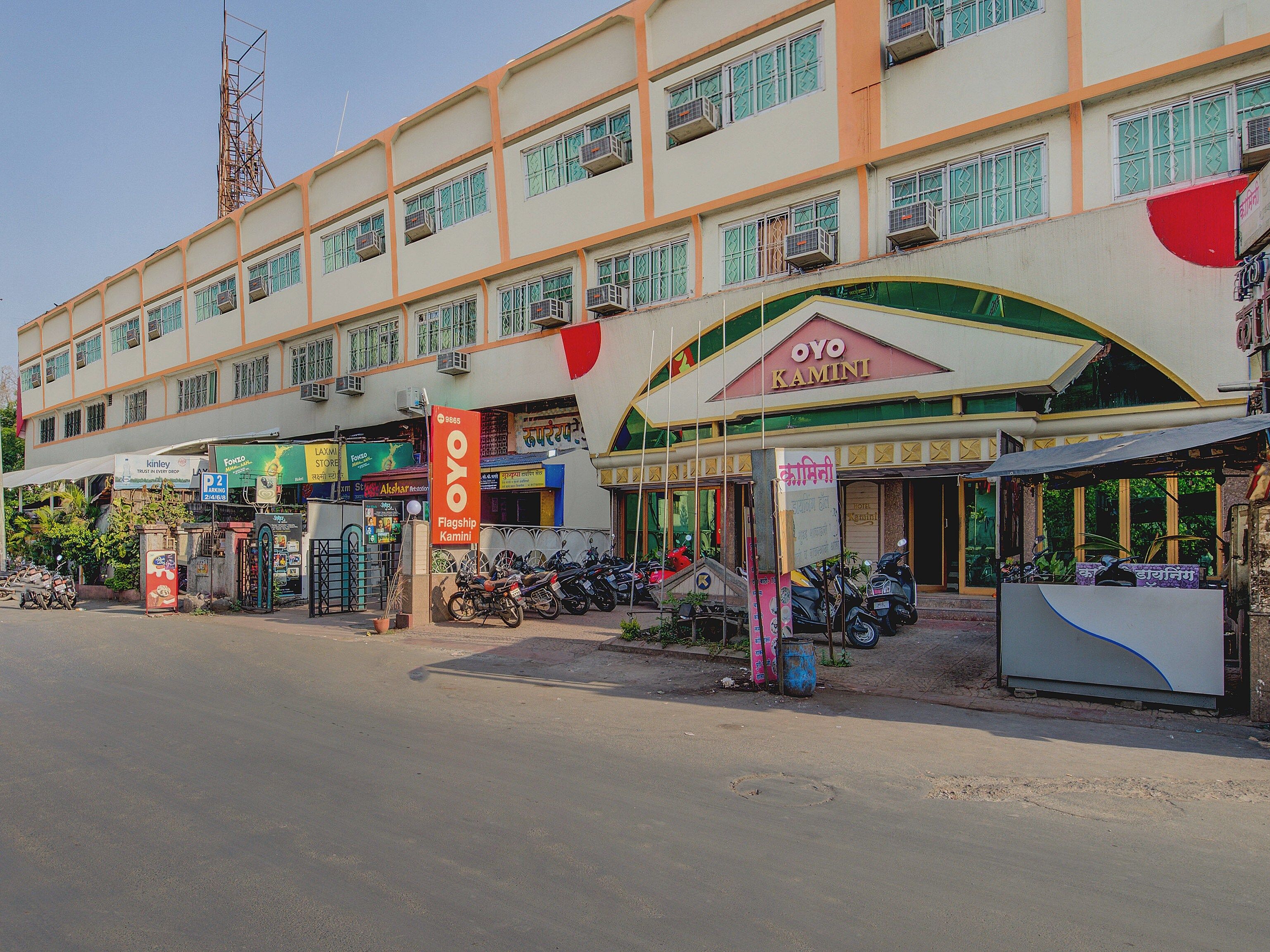 A multi-story building with a prominent OYO Kamini sign, several storefronts, and parked motorcycles.
