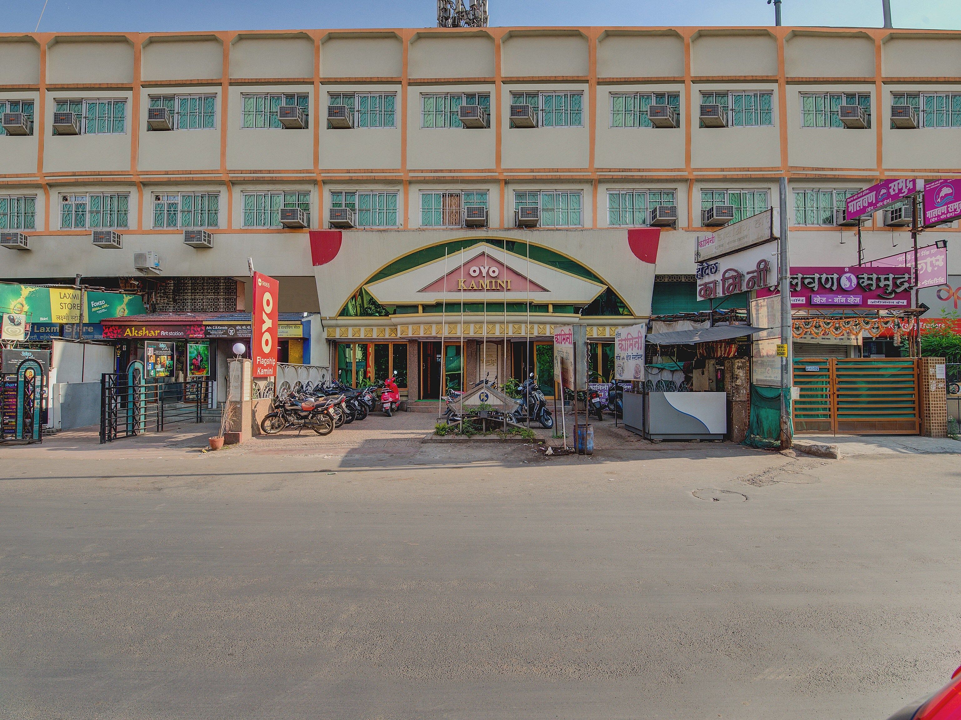 A multi-story building with a central entrance, surrounded by various shops and parked motorcycles.