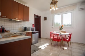 A modern kitchen with a dishwasher, microwave, and a dining area with red chairs and a white table. - Villa Kalimera - Three Bedroom Villa, Sleeps 6 (Gennadi)