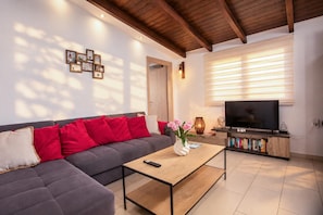 A modern living room with a sofa, coffee table, TV, and bookshelf. - Villa Kalimera - Three Bedroom Villa, Sleeps 6 (Gennadi)