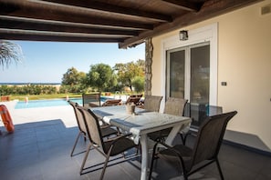 Un área de comedor al aire libre techada con piscina y vista al océano.