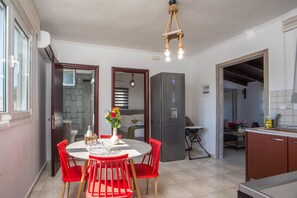 A compact kitchen with a dining area, a refrigerator, and a hanging light fixture. - Villa Kalimera - Three Bedroom Villa, Sleeps 6 (Gennadi)