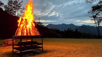 A campfire with a metal table in a grassy field with mountains in the background.