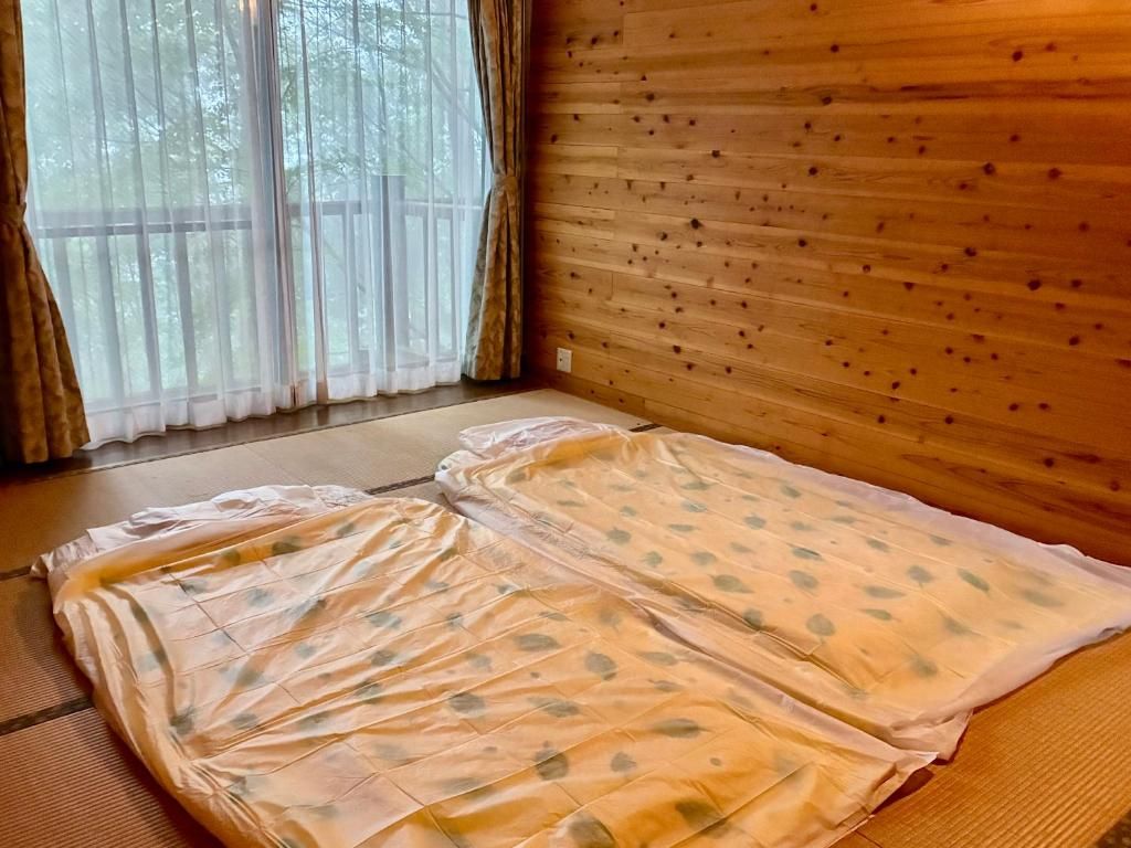 Una habitación con esteras de tatami, pared de madera y ventana con cortinas.
