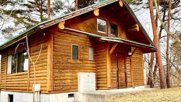 Eine Blockhütte mit steilem Dach, einer Veranda und einem kleinen Fenster.