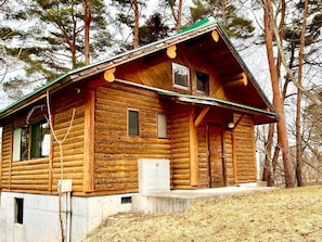 A log cabin with a steep roof, a front porch, and a small window.