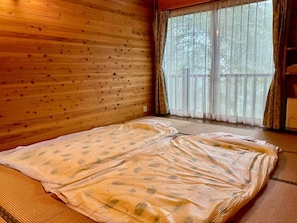 A room with a large bed, wooden walls, and a view through a window. - YOKOTE FOREST BASE (Aoki)