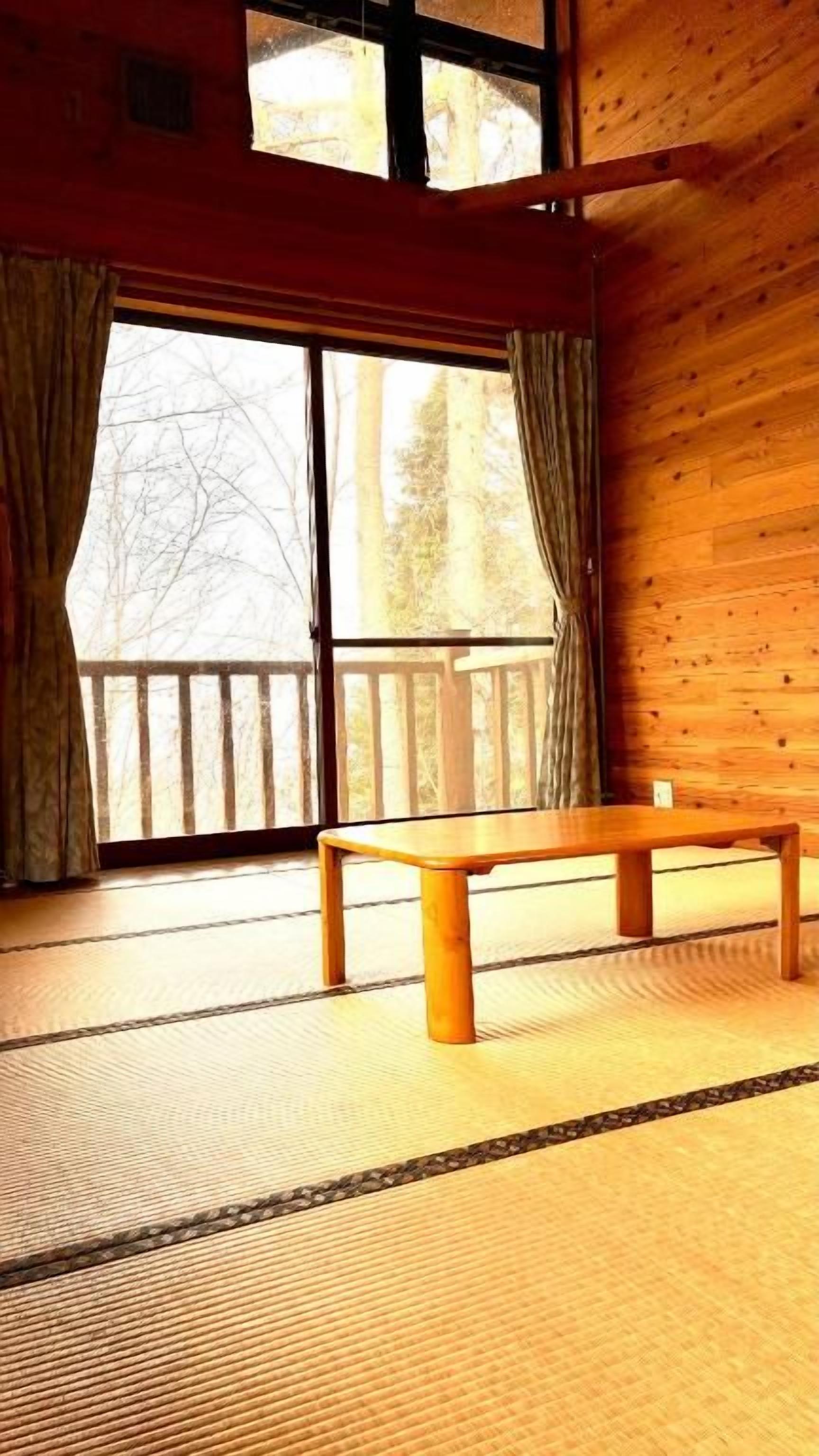 A room with tatami flooring, a wooden bench, and a large window with curtains.