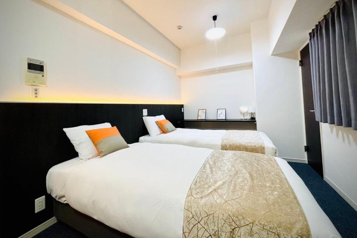 Une chambre d’hôtel avec deux lits, un luminaire au plafond, un thermostat et une fenêtre avec des rideaux.