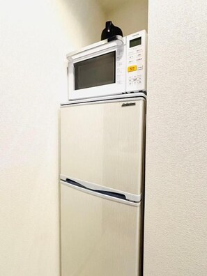 Un réfrigérateur blanc, surmonté d’un four à micro-ondes, est placé dans un coin d’une pièce dont le mur est texturé.