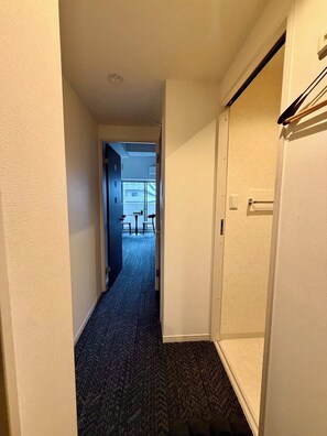 Un couloir étroit, dont le sol est recouvert de moquette, mène à une pièce dotée d’une porte.