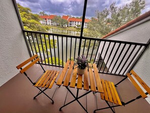 Ein Balkon mit Holztisch und -stühlen, einem Blumentopf und Blick auf Gebäude und Bäume.