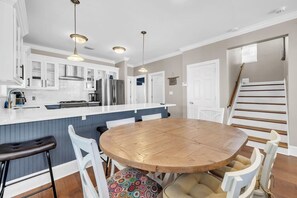 Une cuisine moderne avec des meubles blancs, un réfrigérateur en acier inoxydable et une table à manger en bois, assortie de chaises blanches.