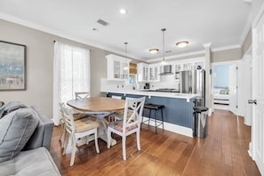 A modern kitchen with white cabinetry, stainless steel appliances, and a wooden dining table with chairs. - 🚲Sugar Sand Bungalow | Pet Friendly | Bikes | Spacious Balcony | Walk to Beach🐾 (Santa Rosa Beach)