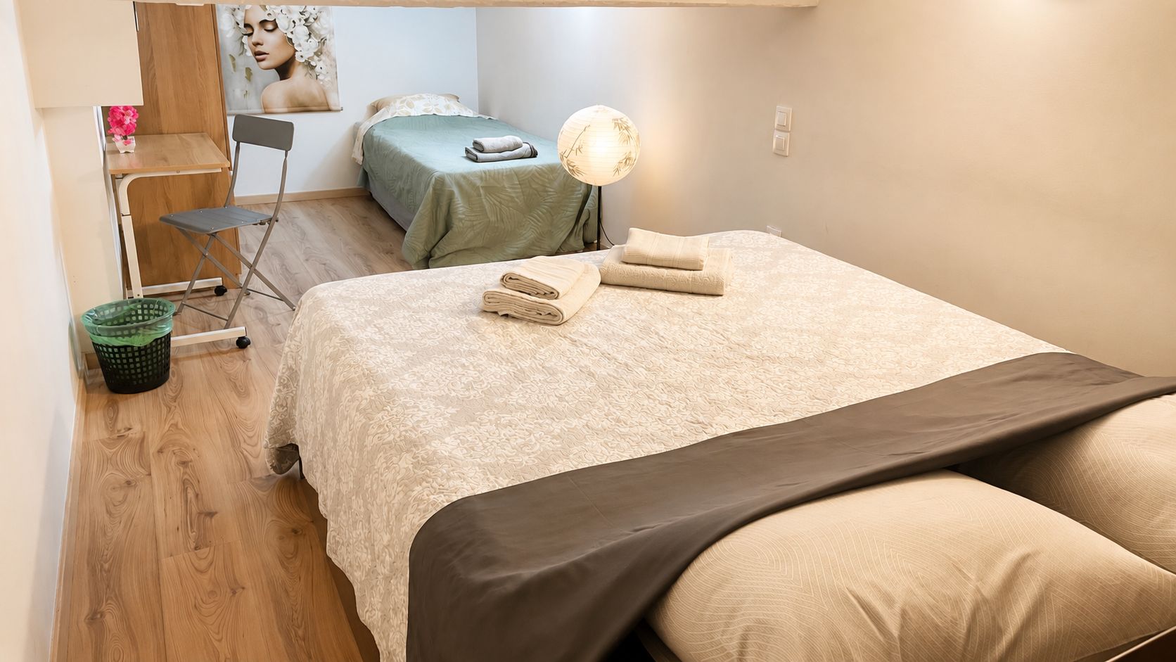A bedroom with a bed, a chair, a desk, a lamp, and a wall-mounted shelf.