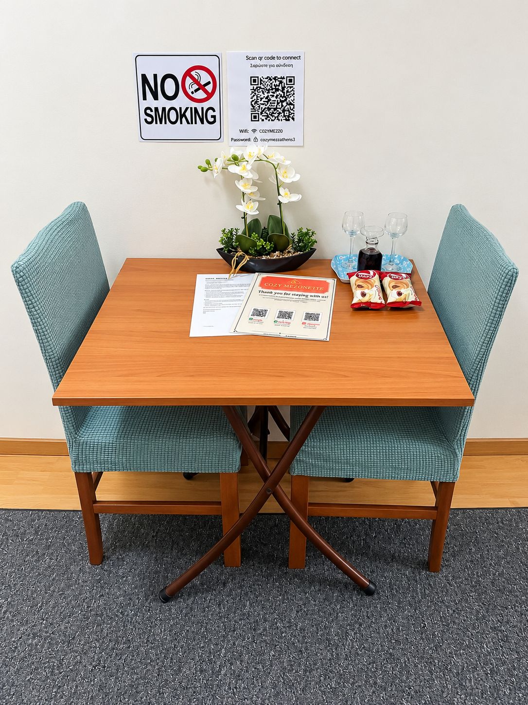 Una mesa de comedor con un cartel de 'NO FUMAR', un código QR para Wi-Fi y una tarjeta de agradecimiento que dice 'COZY MEZONETTE'.